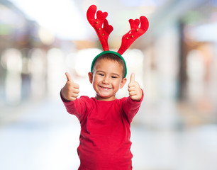 portrait of a little boy wearing a reindeer headband and doing the okay gesture