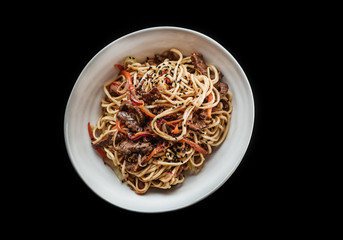 Egg noodles with beef and vegetables in a white plate on a black background. Healthy Asian cuisine. Top view. Toned image