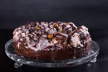 chocolate cake with nuts coated with a glaze on a black background, studio
