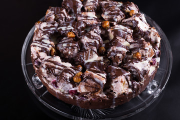 chocolate cake with nuts coated with a glaze on a black background, studio