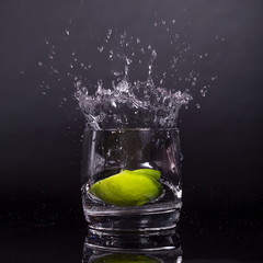 Falling in a glass of lemon, lime, splash on black background, isolated, water drop