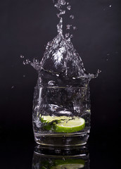 Falling in a glass of lemon, lime, splash on black background, isolated, water drop