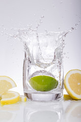 Splashes of water, lemon lime falling into a glass, isolated, reflection, white background, water drop