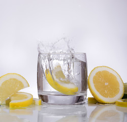 Splashes of water, lemon falling into a glass, isolated, reflection, white background, water drops
