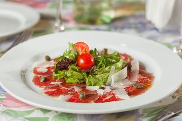 meat with tomatoes, cheese and capers on a white plate