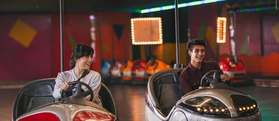 Tuinposter Amusementspark Two young friends riding bumper cars at amusement park