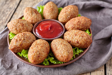 Kibbeh traditional middle eastern homemade beef, lamb, goat or camel meat stuffed bulgur kofta spicy meatball croquettes on green salad food on vintage wooden table background