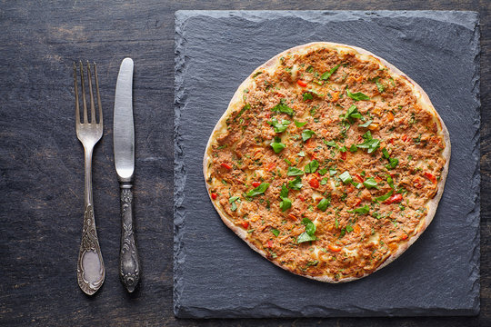 Lahmacun traditional turkish pizza with minced meat, paprika tomatoes, parsley baked spicy food on dark table background