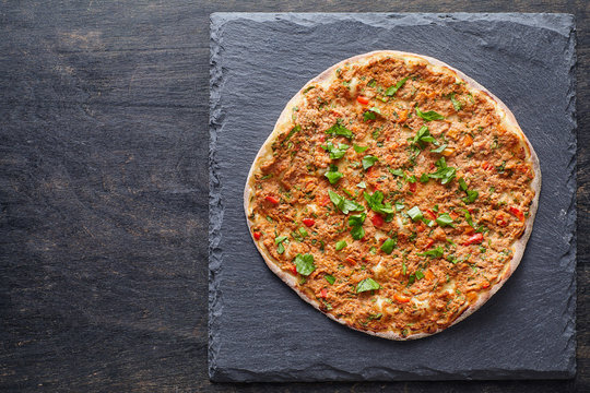 Lahmacun turkish gourmet pizza with minced beef or lamb meat, paprika, tomatoes, cumin spice, parsley baked spicy middle eastern food on dark table background
