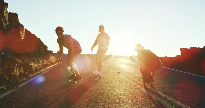 Skateboarders bombing down steep hill at sunset