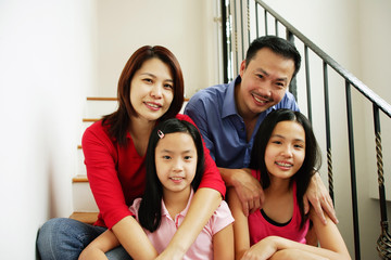 Family of four sitting on stairs, looking at camera, family portrait