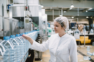 Young happy woman worker in factory checking water gallons before shipment.