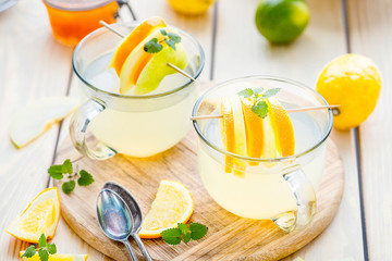 Two Cups of Hot Spiced Tea with Lemon, Orange and Apple on Light Wooden Table