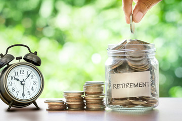 Hand putting Coins in glass jar with retro alarm clock , retirement