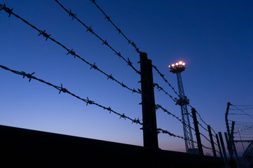 Barbed wire and electric lamp against blue sky at night