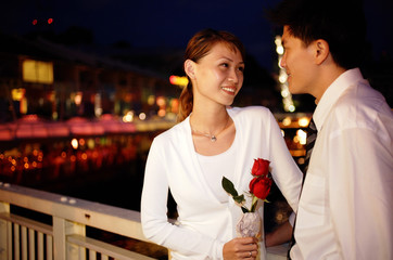 Couple standing face to face, woman holding single rose stalk