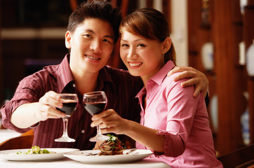 Couple in restaurant, looking at camera, toasting with wine glasses