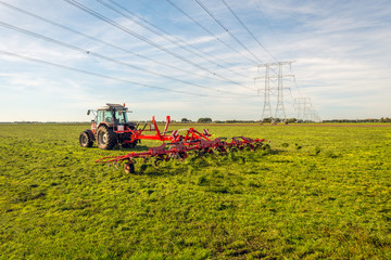 Hay tedding in a Dutch landscape with high voltage pylons and lines