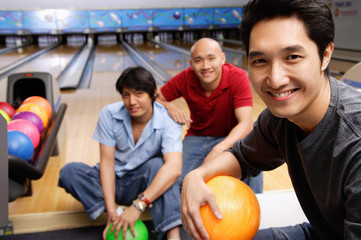 Three men in bowling alley, smiling at camera