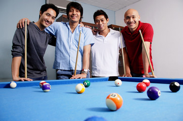 Men standing around pool table, looking at camera