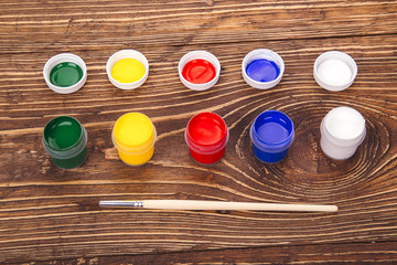 acrylic paints in jars near the brush, on the retro wooden backg