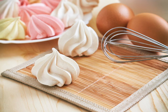 Fresh delicious colored meringue cookies on wooden table with eggs and whisk in background
