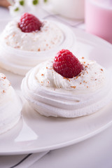 Meringue nests topped with whipped cream and raspberry  on a whi