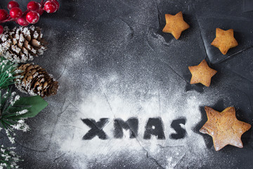 christmas background with branch of christmas tree and baked gingerbread stars with word Xmas made from powdered sugar. creative idea