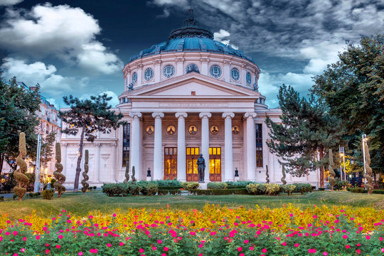 Romanian Atheneum at sunset with red and yellow flowers in front.Blue sky. Bucharest, Romania.