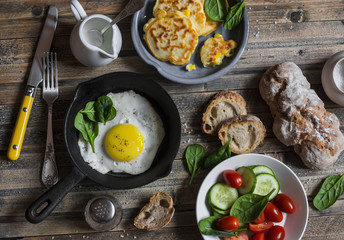 Snack or breakfast table - fried egg, corn fritters, vegetables, homemade bread on wooden background, top view