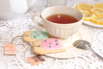 A cup of tea and sugar cookies (cookies as imitation of teabags) served on a lace tablecloth, teatime. Selective focus