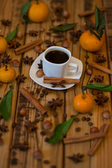 Small white cup of coffee, cinnamon sticks, cocoa beans, star anise, hazelnuts and mandarins on wooden background