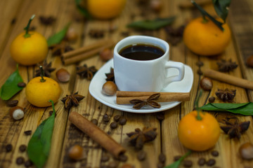 Small white cup of coffee, cinnamon sticks, cocoa beans, star anise, hazelnuts and mandarins on wooden background