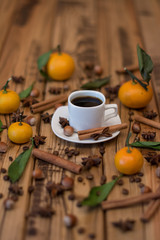 Small white cup of coffee, cinnamon sticks, cocoa beans, star anise, hazelnuts and mandarins on wooden background