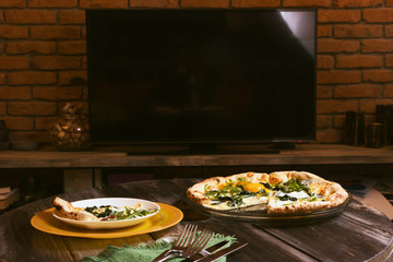 Pizza on background of the plasma television. Art background, tableware, home interior