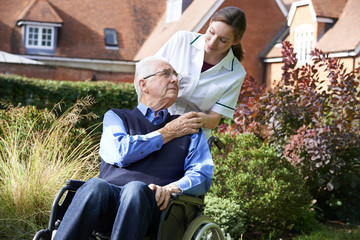 Carer Pushing Senior Man In Wheelchair