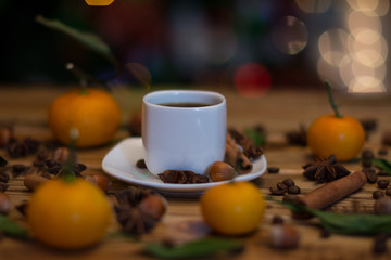 Small white cup of coffee, cinnamon sticks, cocoa beans, star anise, hazelnuts and mandarins on wooden background