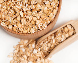 Oat flakes in wooden bowl and scoop on white background. Close up, top view, high resolution product