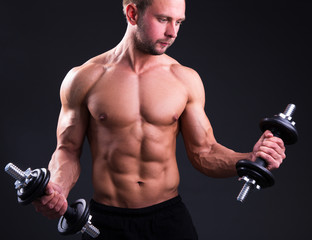 muscular man posing with dumbbells over grey
