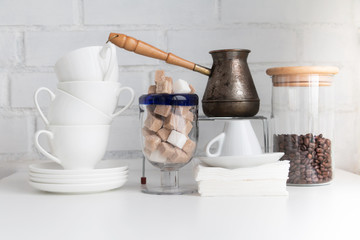 Coffee drink concept. Coffee cups, jezve, coffee beans, sugar cubes, cane sugar, white sugar and white porcelain cups. Piece of cafe or restaurant interior.