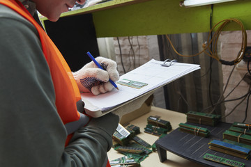 Worker in computer recycling plant noting down RAM serial numbers