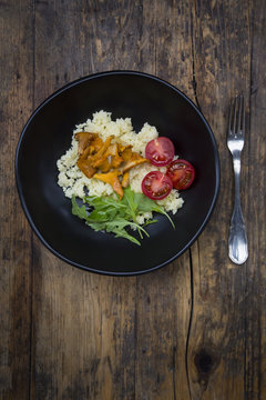 Bowl of couscous salad with tomatoes, rocket and chanterelles on wood