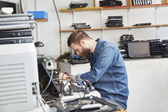 Worker in computer recycling plant removing accus from laptop