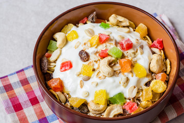 Healthy breakfast with yogurt, muesli and candied fruit in ceramic bowl on stone background