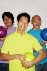 Three men holding bowling balls, smiling at camera