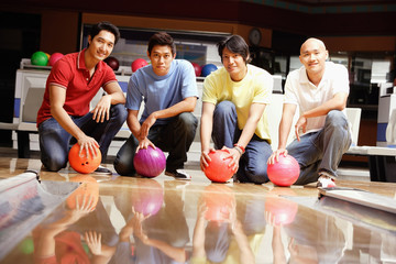 Four men crouching in bowling alley, holding bowling balls