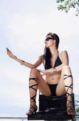 Woman in bikini and high heels, sitting in chair, holding mobile phone