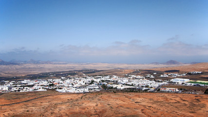 Mountain valley with white buildings and villages between old volcanic slopes. Red Earth and green fields on the background of deep blue sky with white clouds. Lanzarote, Canary Islands, Spain