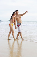Couple walking on beach, holding hands, man pointing to the distance