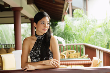 Woman wearing halter top, leaning on railing, arms crossed